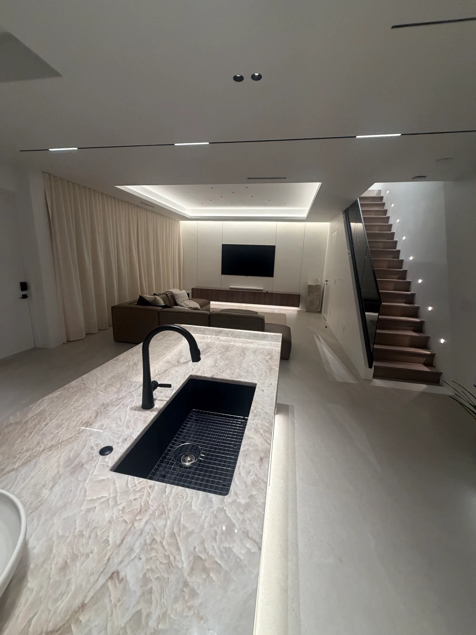 Stone island with a black faucet, the lit stair and living room beyond
