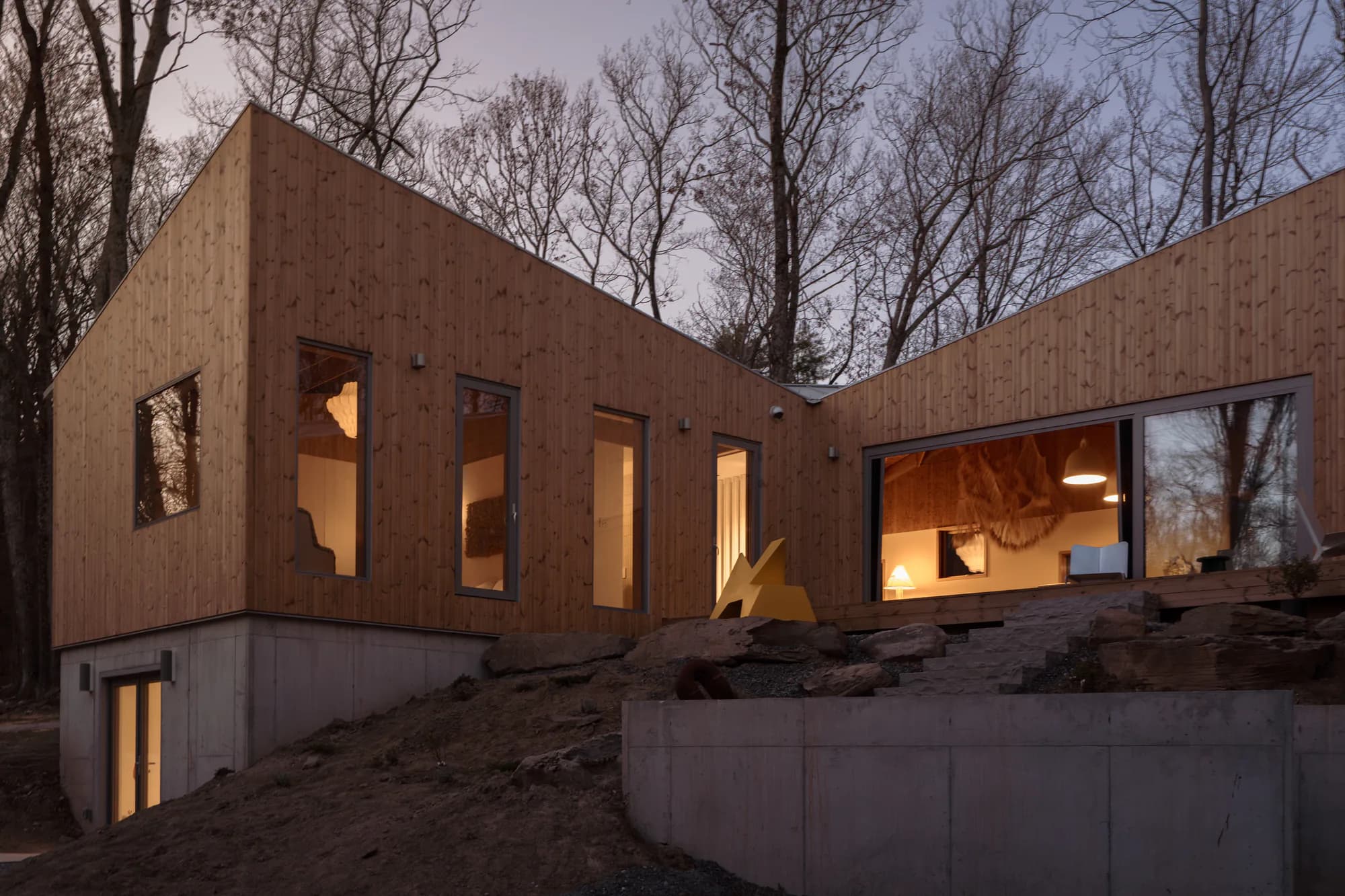 The court side of the house at dusk, interior lit through full-height glazing