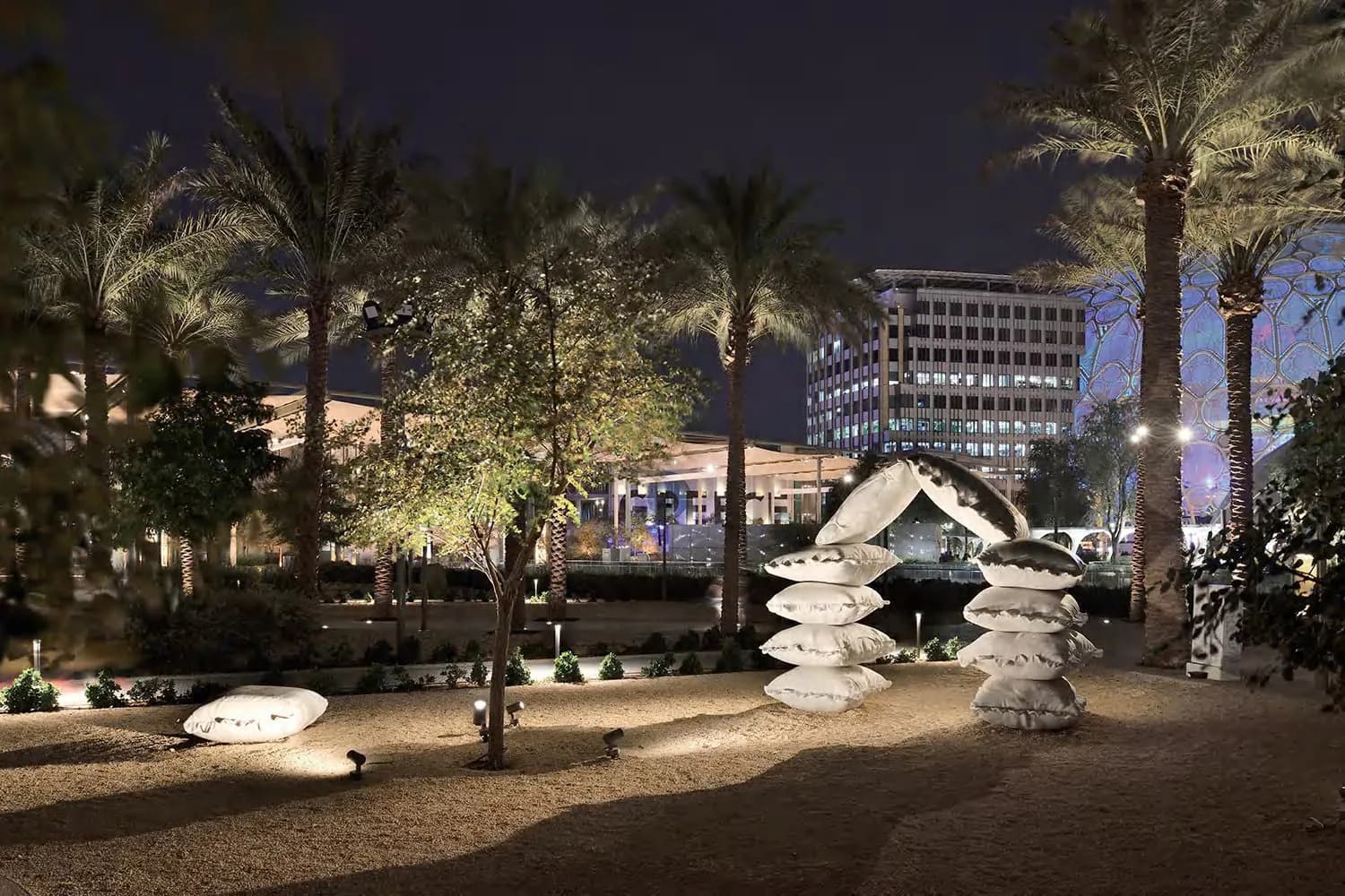 Garden at night with palms and sculptures lit by ground-mounted floodlights