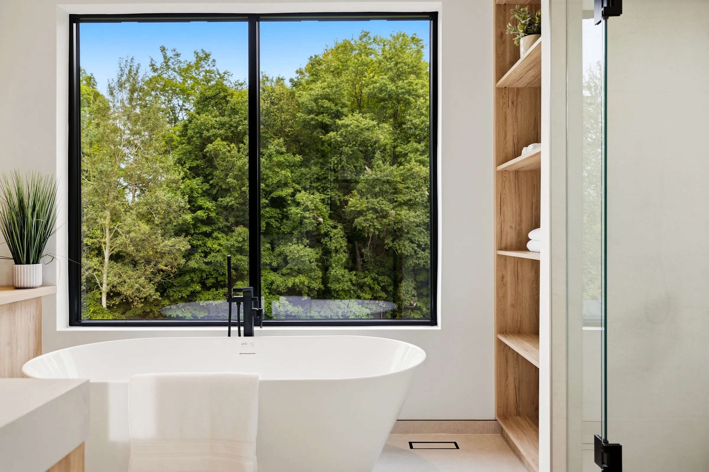 Freestanding tub against the picture window into the trees, lit oak shelving beside
