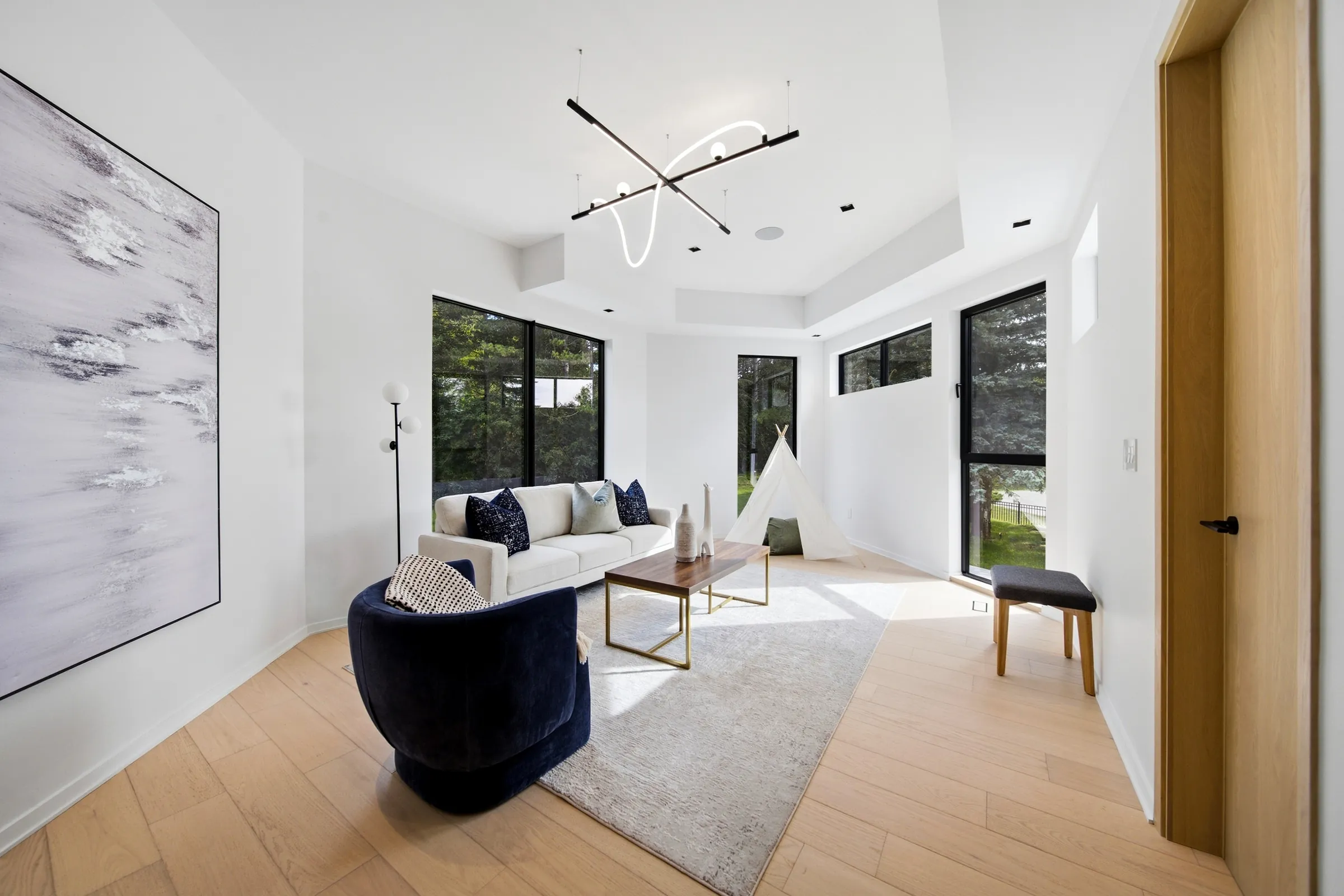 Bedroom sitting area with a linear black pendant and a curved neon loop, black wall sconce beside the art