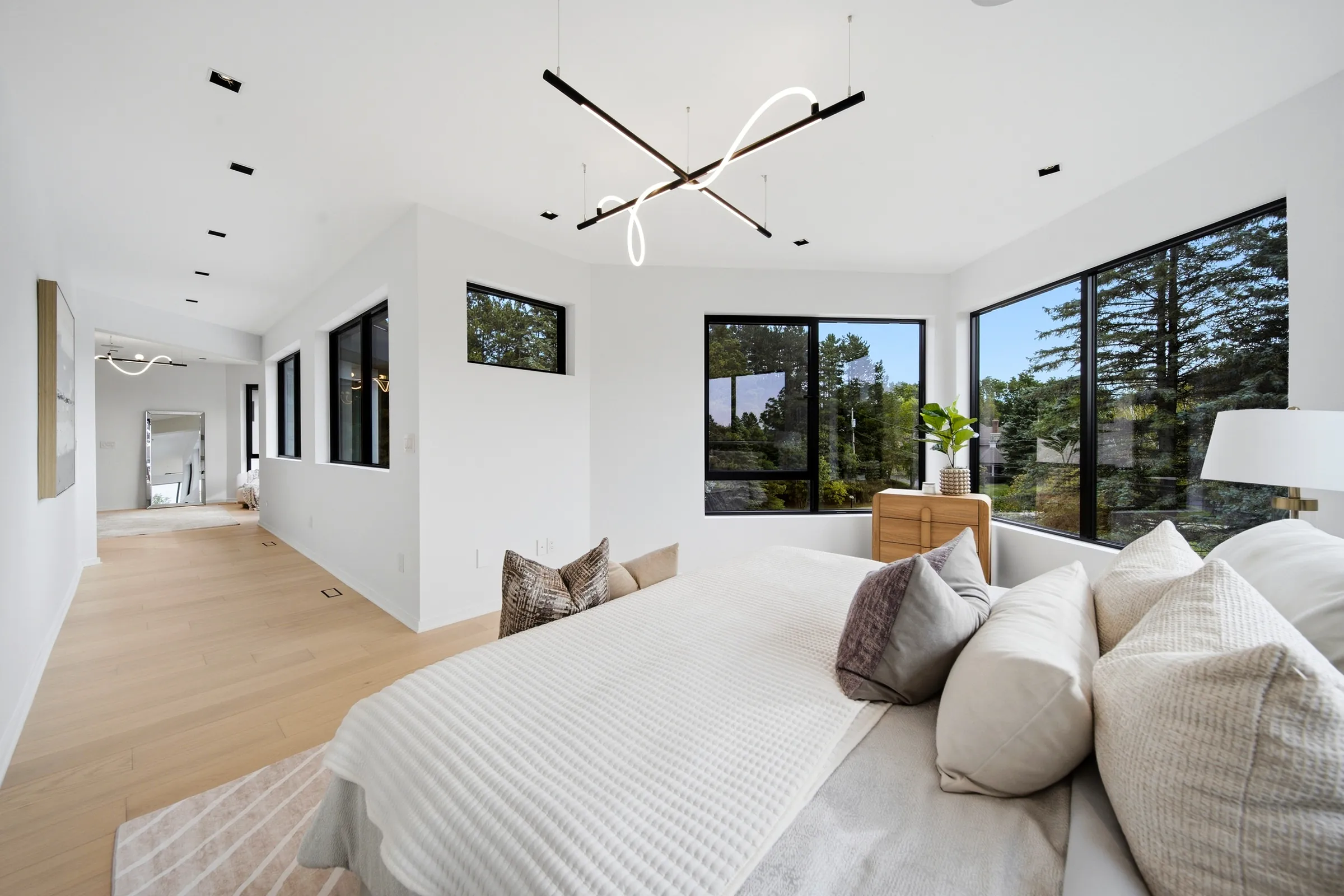 Primary bed under the linear pendant, corner windows into the trees