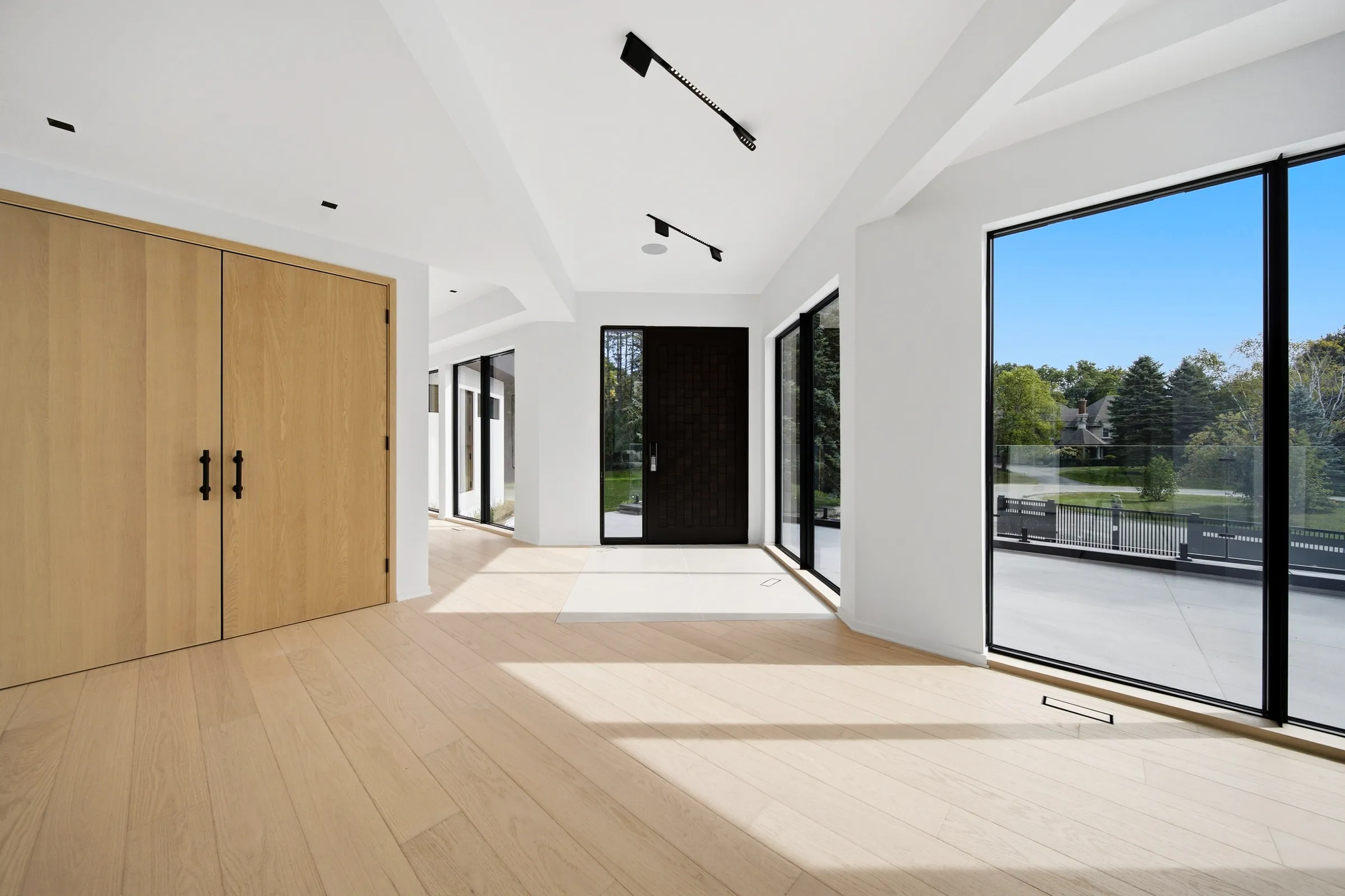 Entry gallery with white oak double doors, surface track spots on the ceiling and the front door beyond