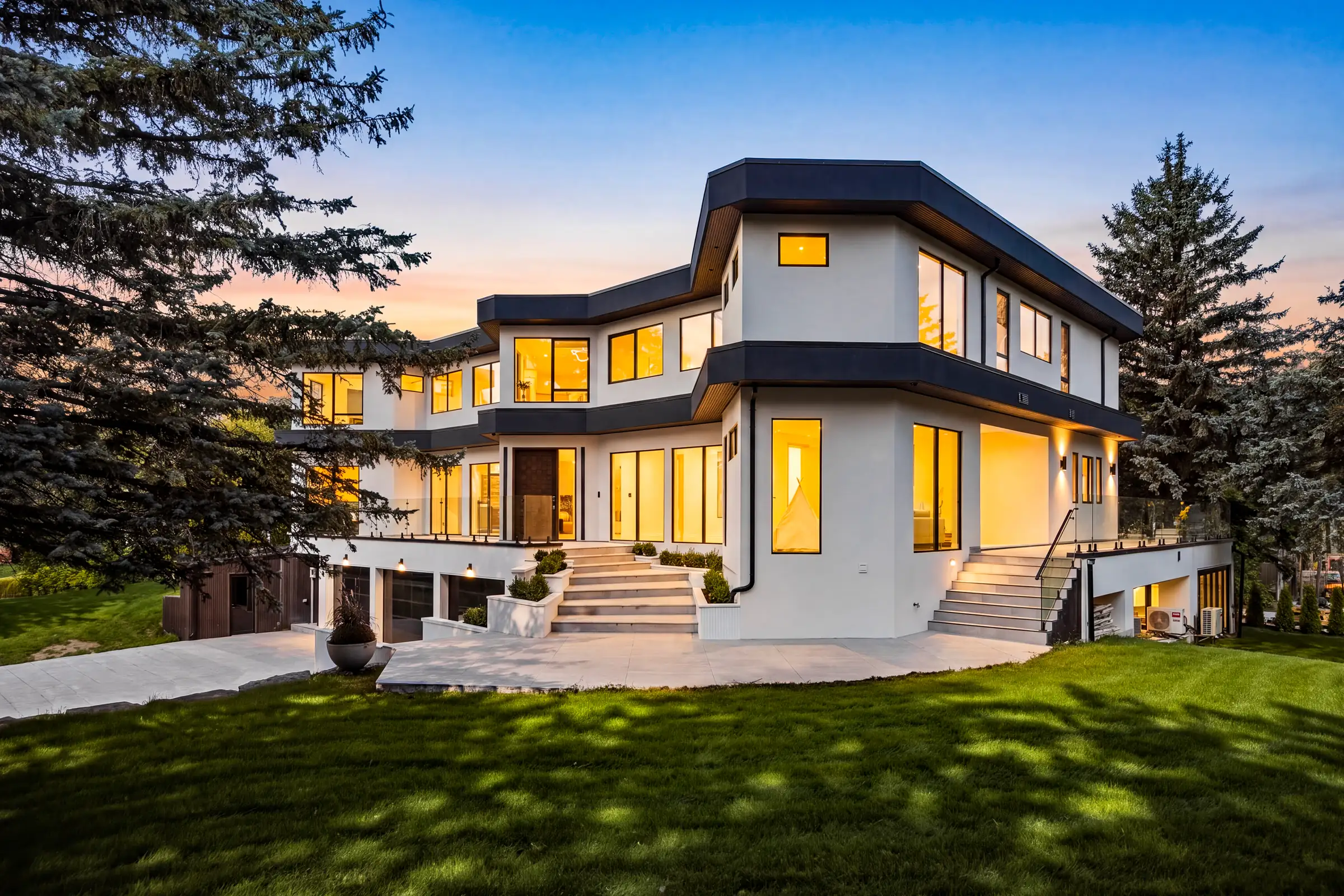Side elevation at dusk across the lawn, entry steps and a lit lower terrace under the angled upper storey