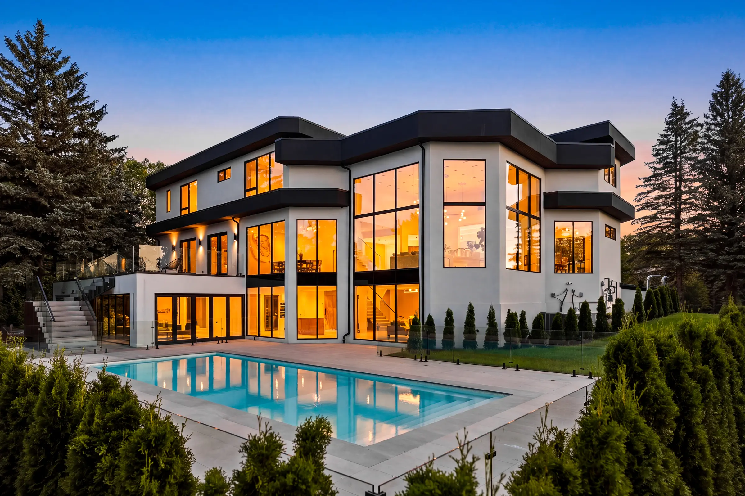 Rear of the house at dusk with the pool in the foreground and the two storey great room window wall lit warm