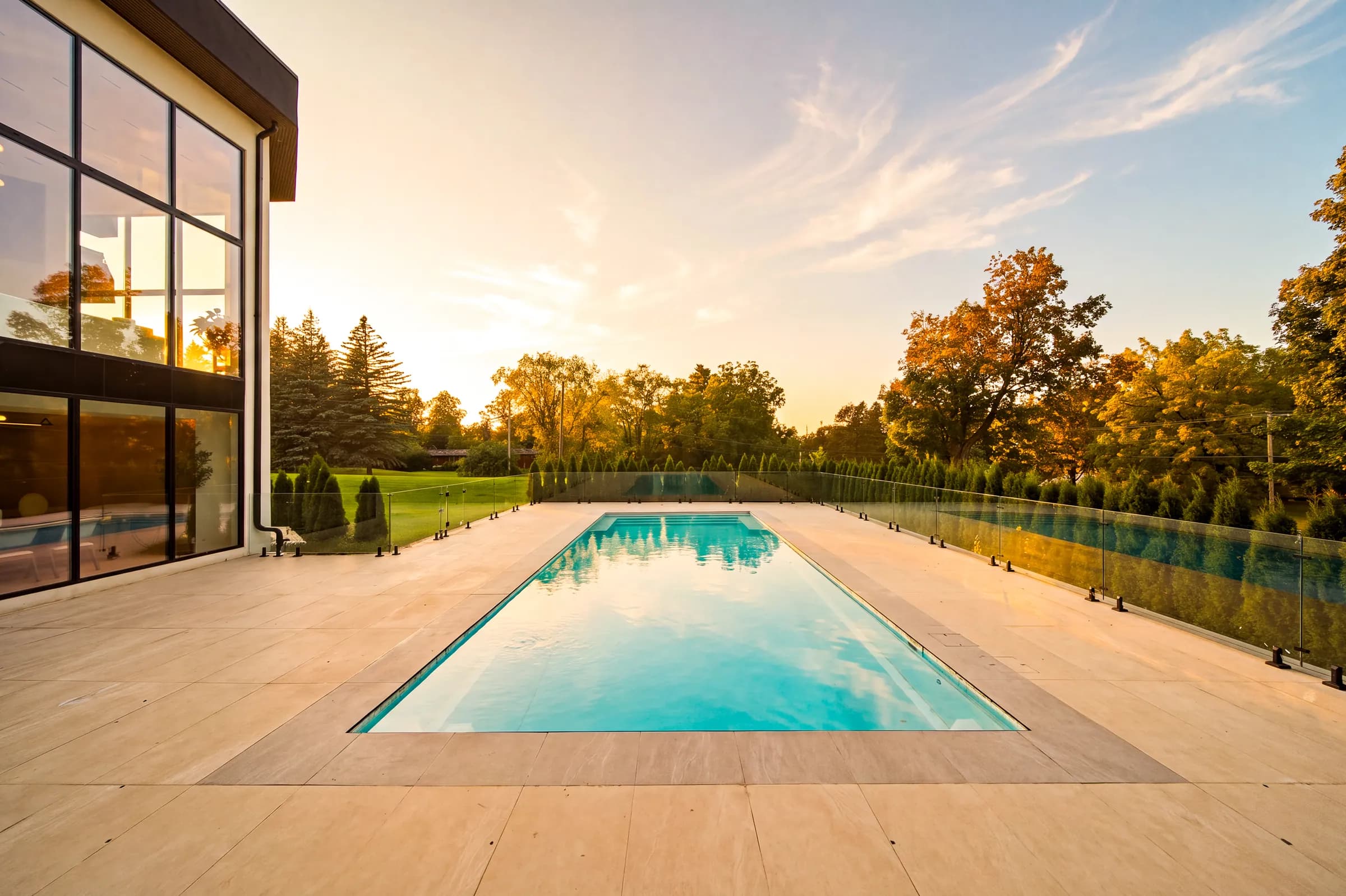Long pool at sunset from the terrace, sky reflected in the water beside the glazed corner of the house