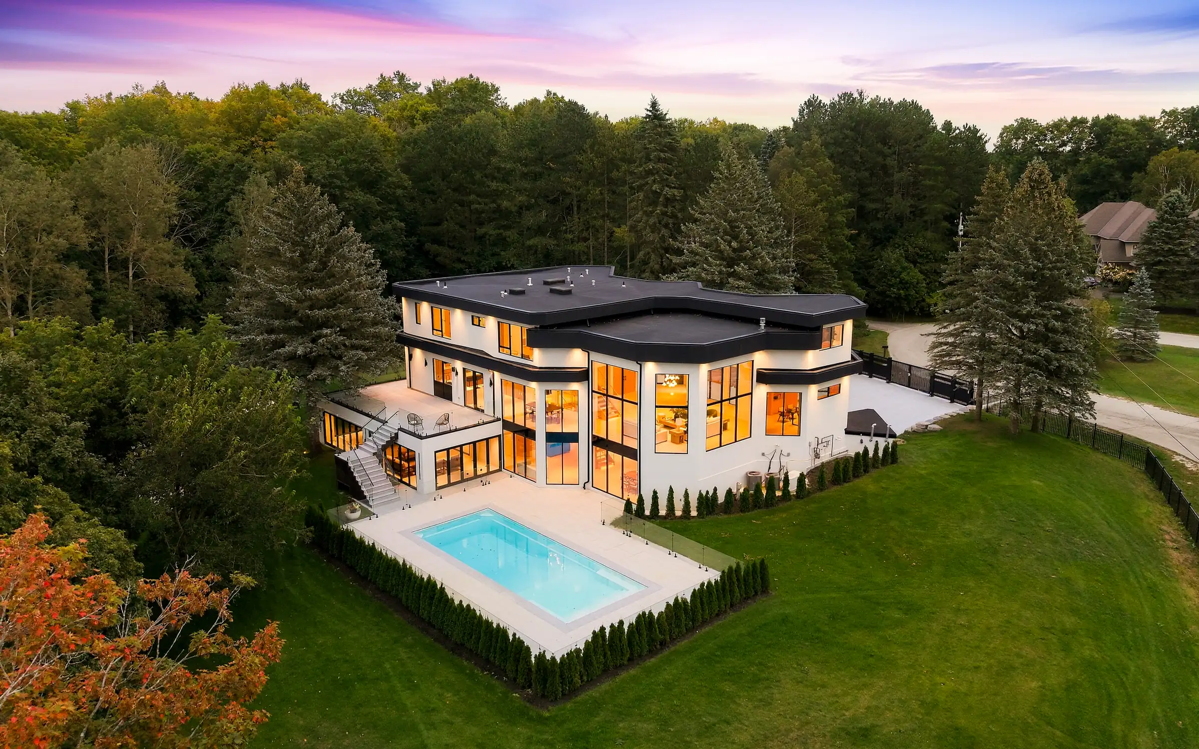 Aerial view at dusk from above the pool, the stepped black roofline and lit upper floor windows