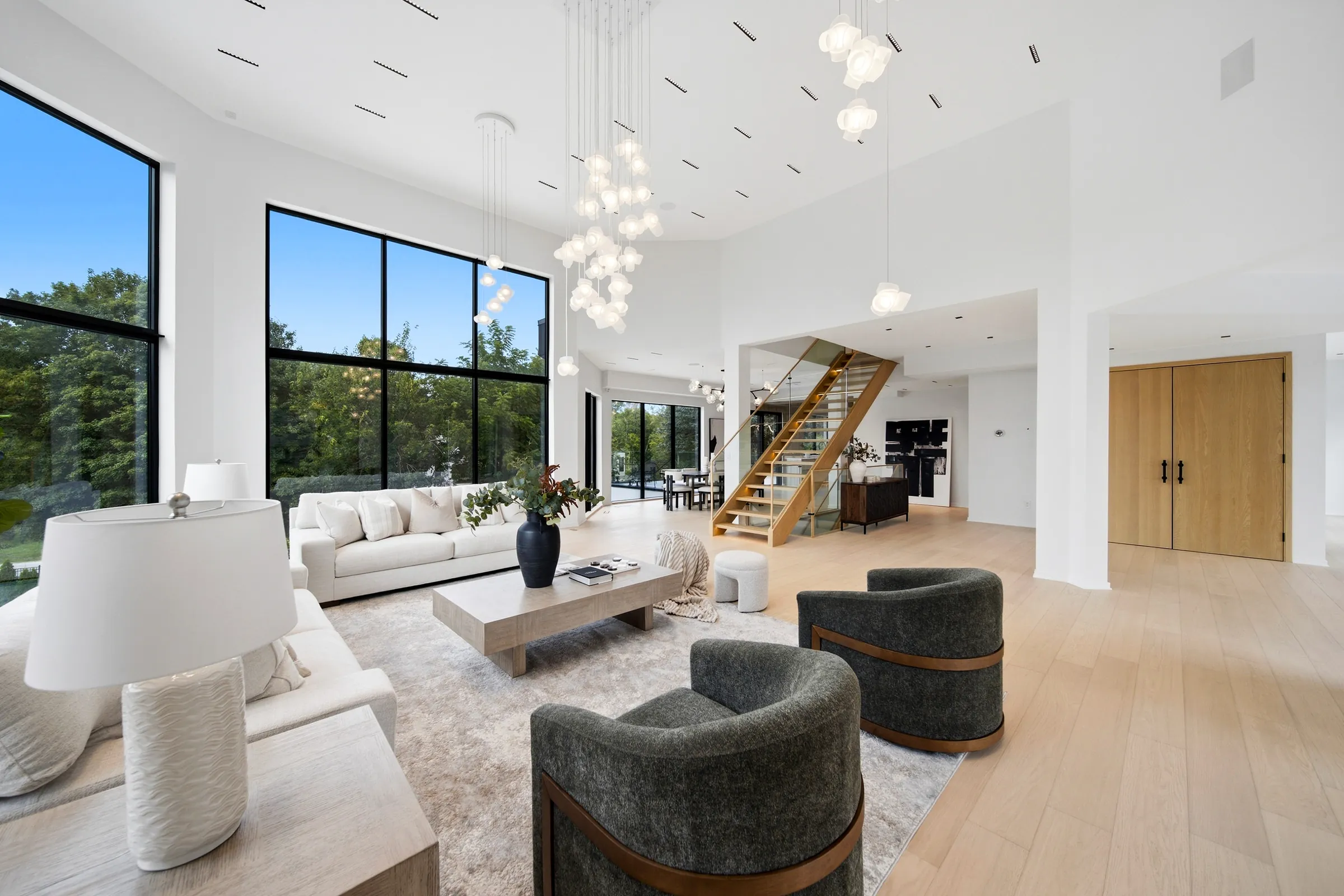 Great room looking toward the open stair and kitchen, pendant cluster above and linear track slots in the ceiling