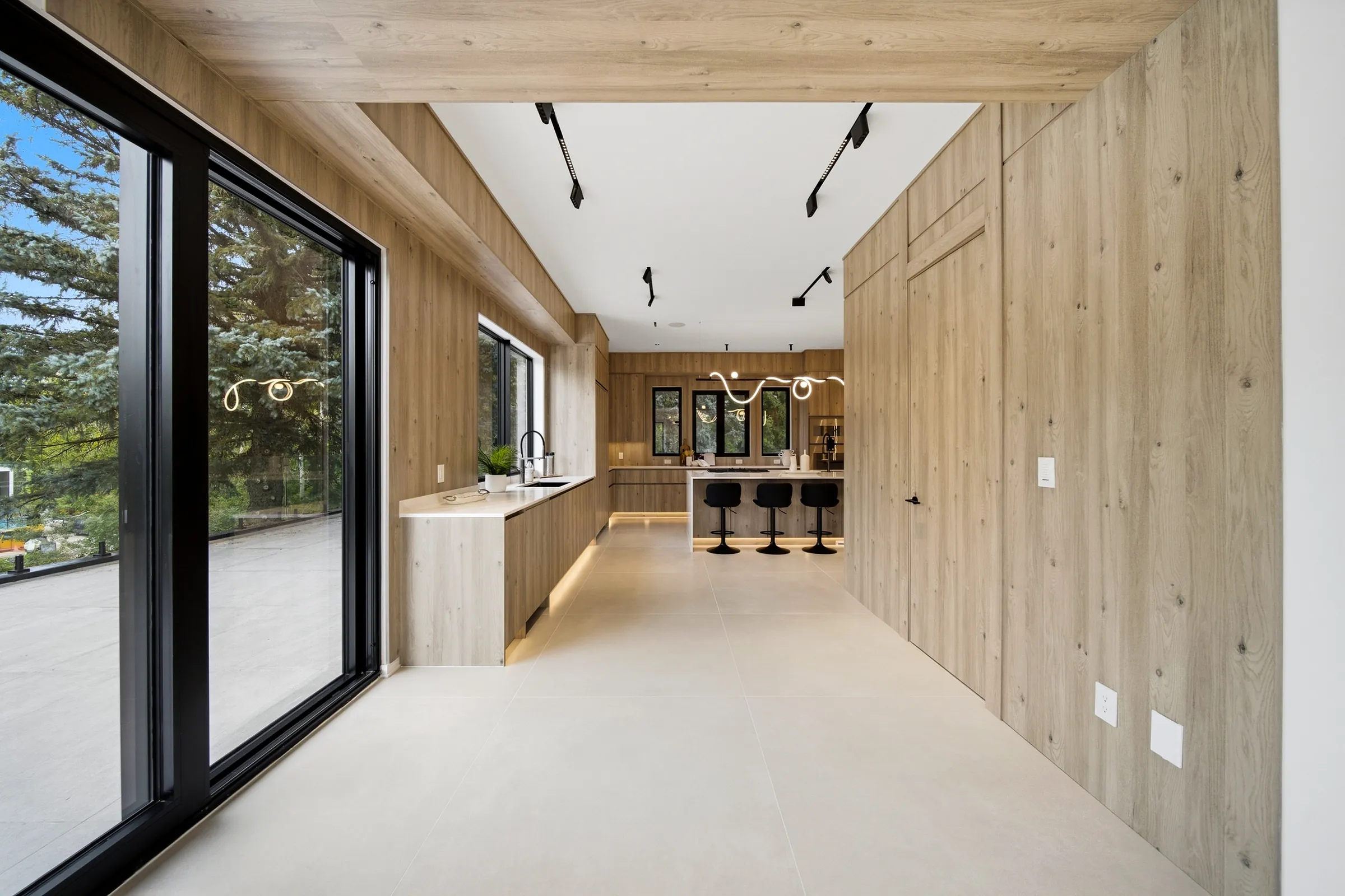 Kitchen approach along the oak panelled wall, ceiling track spots and the looping neon pendant ahead