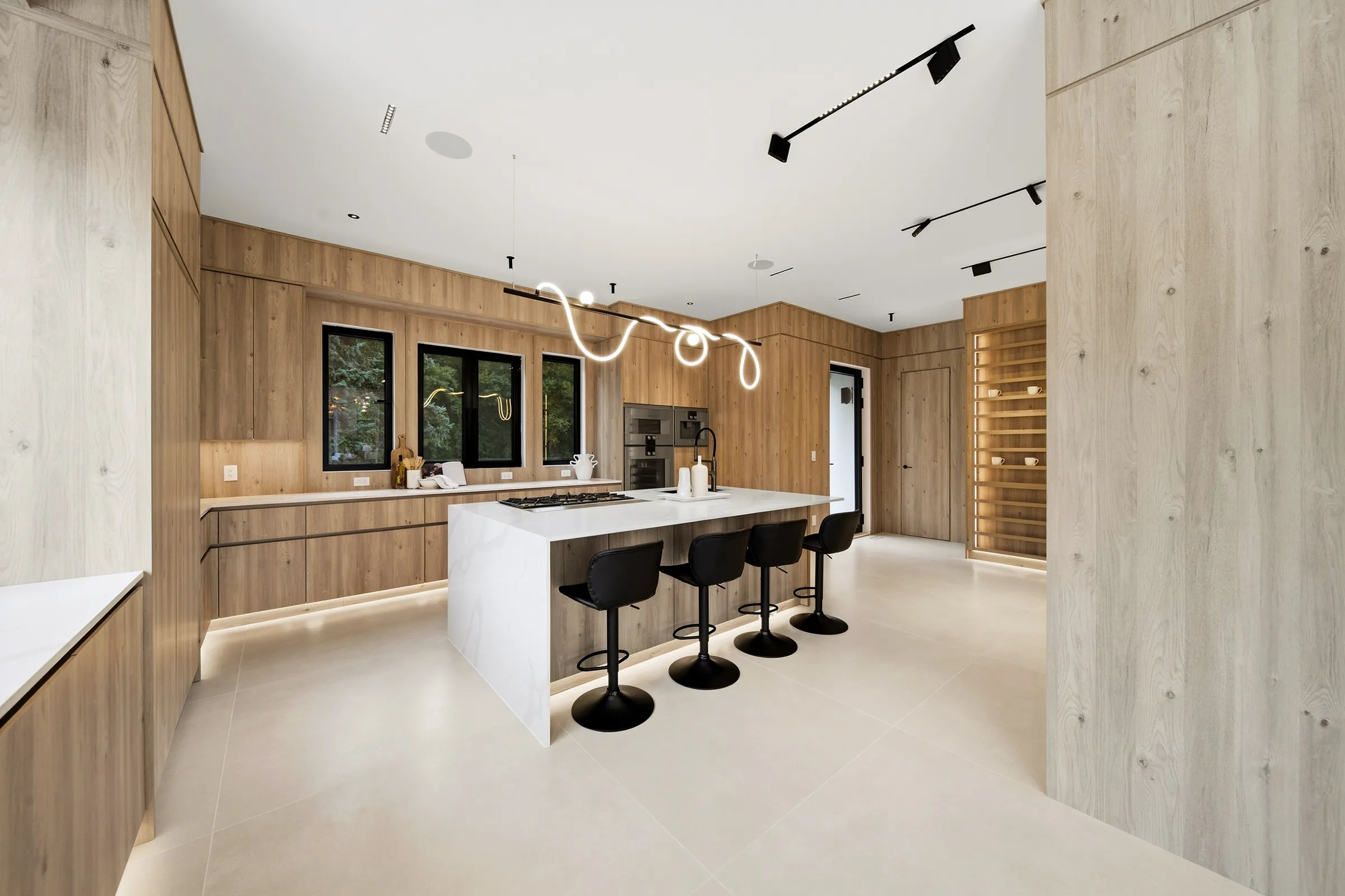 Kitchen island under the looping pendant, lit toe kick plinth and a backlit shelving wall