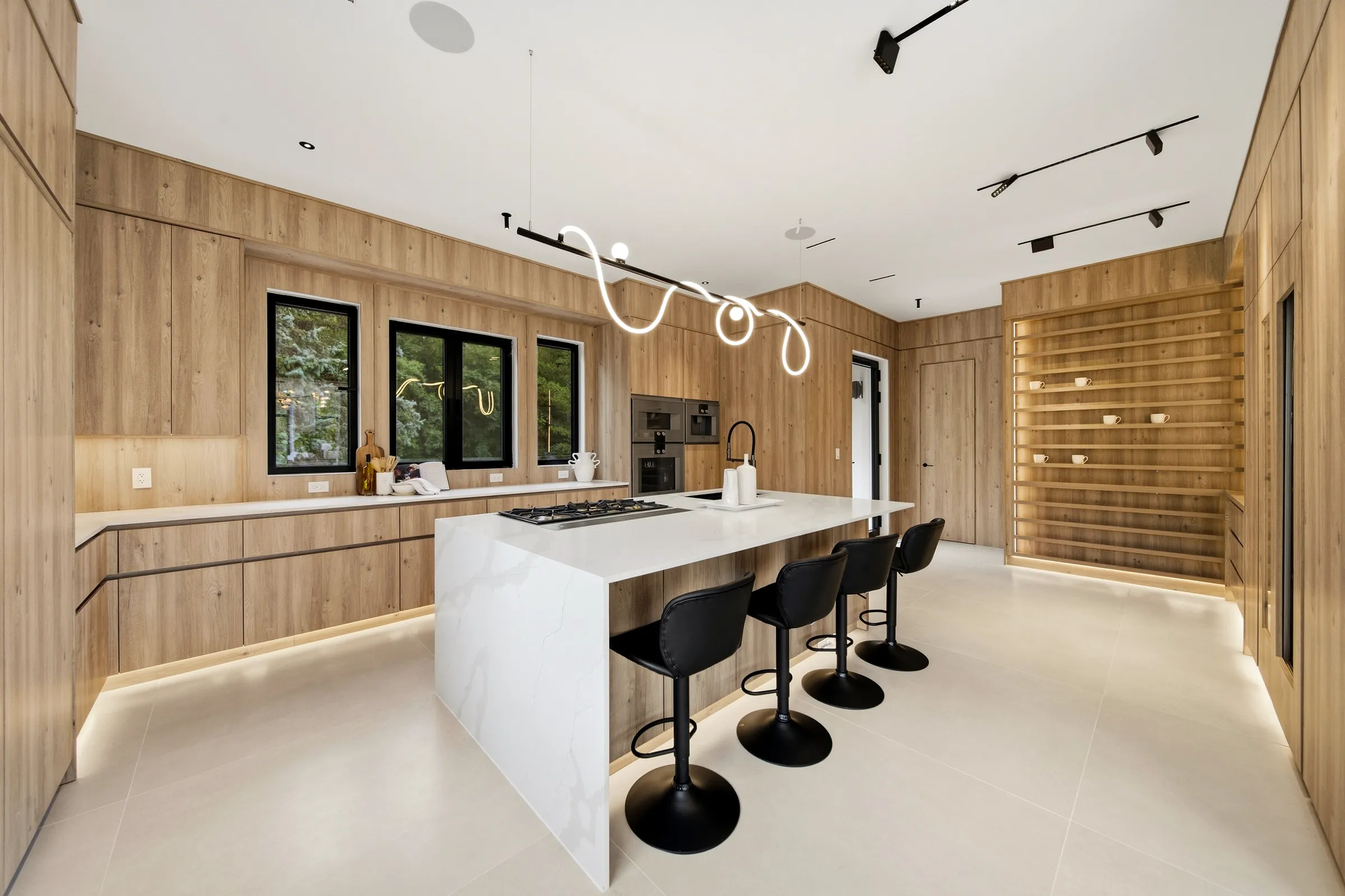 Kitchen with the looping pendant over the island cooktop, track spots and a lit plinth beneath the counters