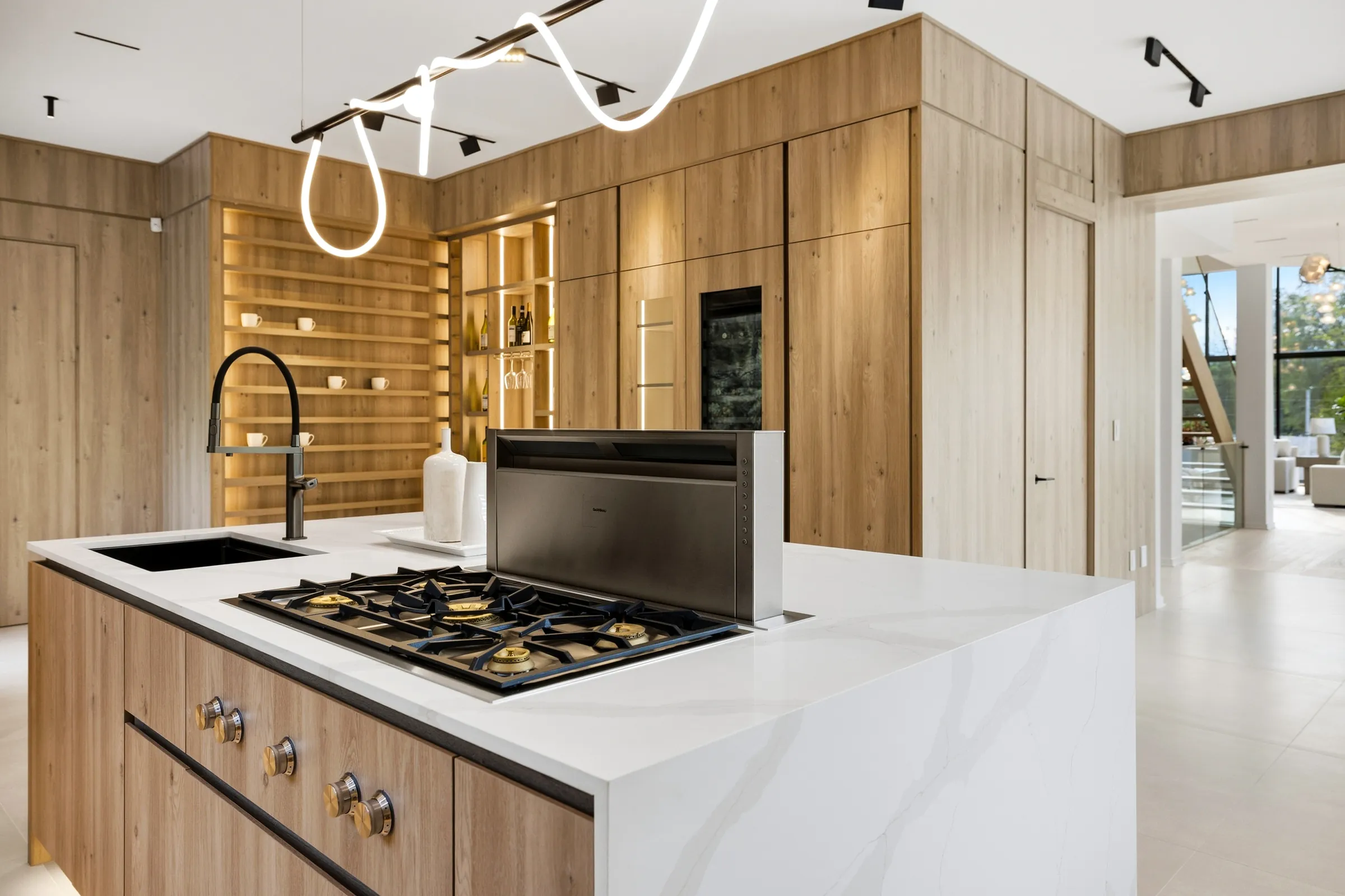 Island cooktop and downdraft with the looping pendant above and backlit oak shelving behind