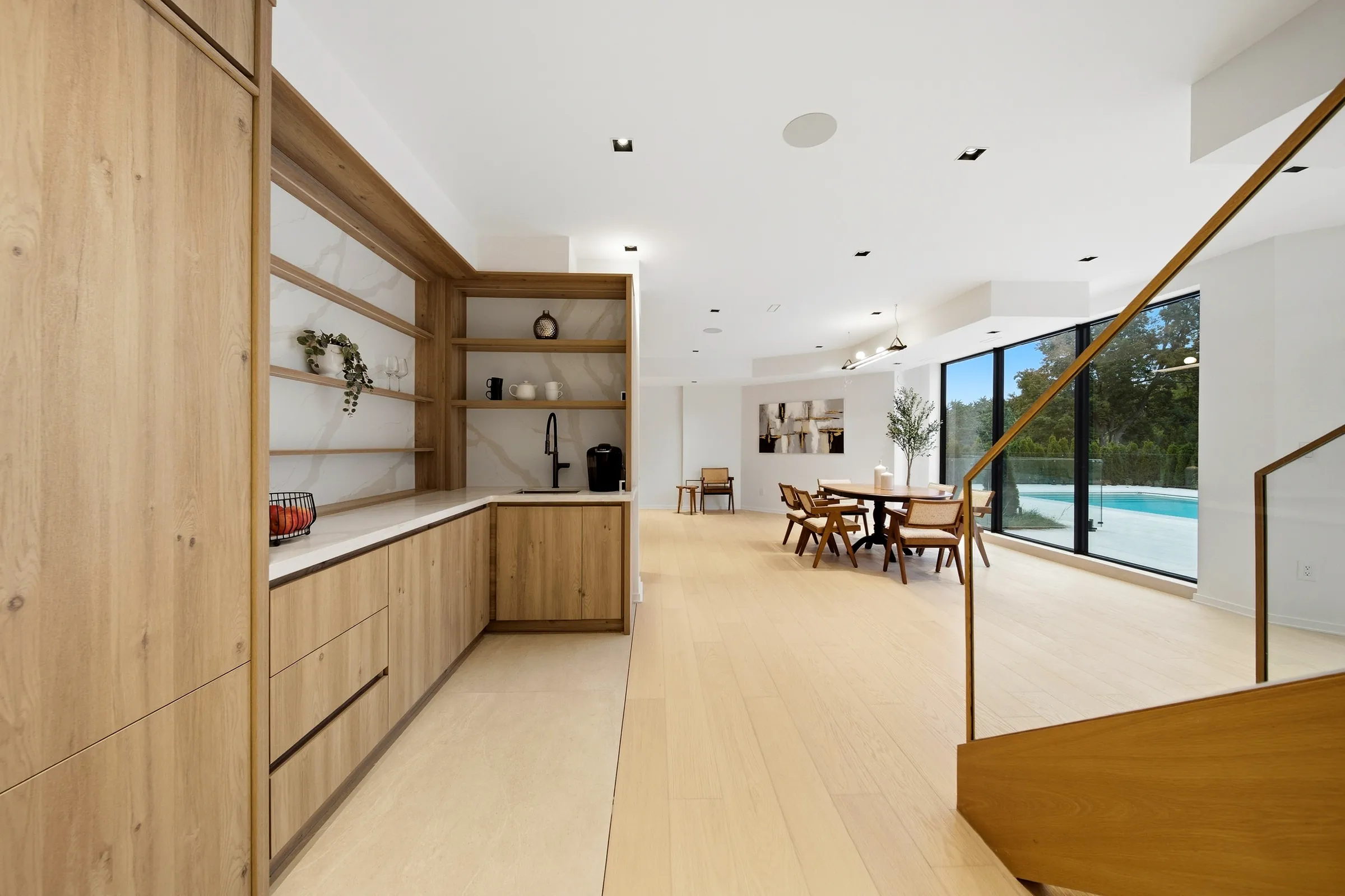 Lower level bar and dining with recessed downlights and the stair rail, pool beyond the glazing