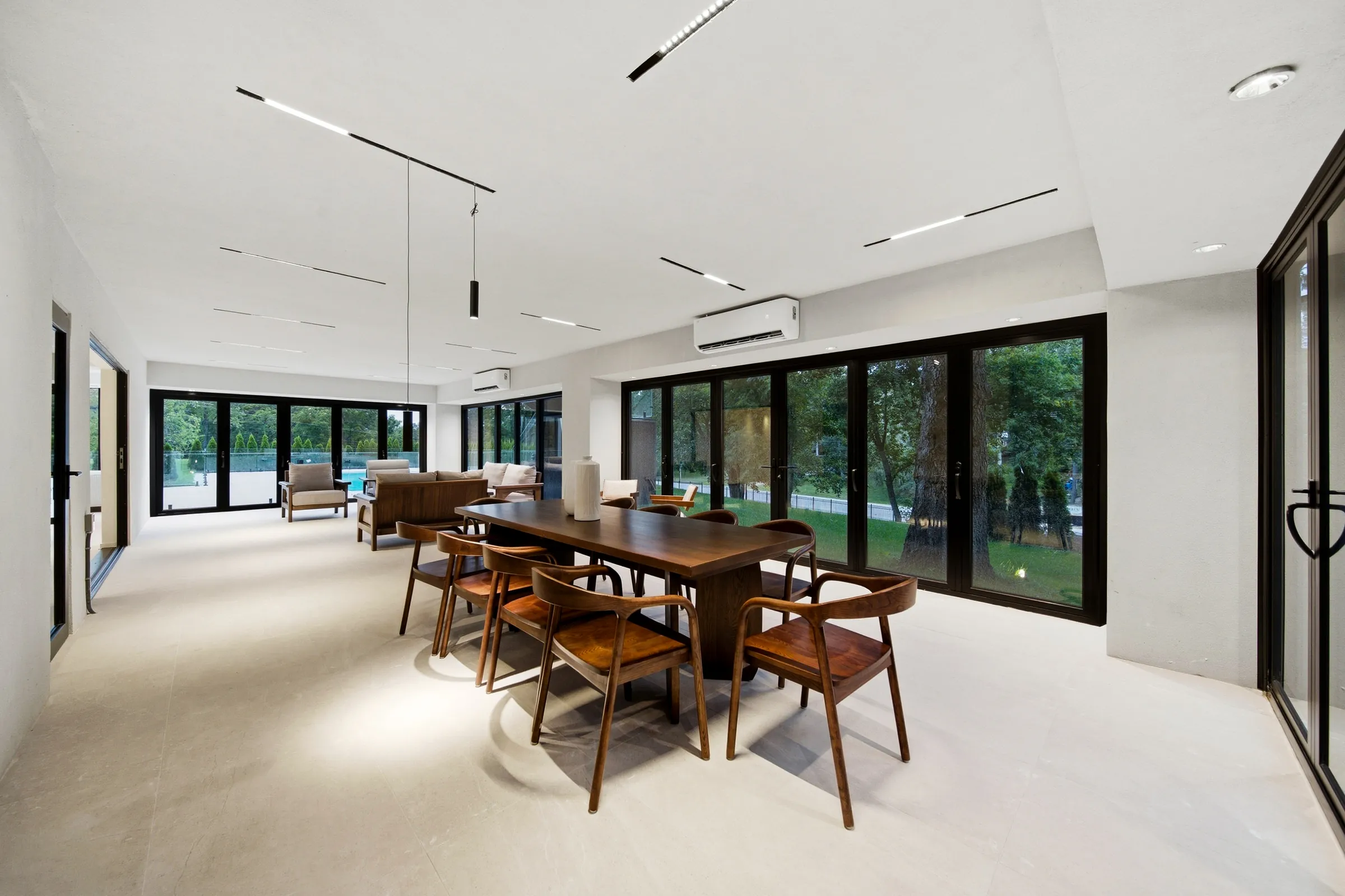 Lower level dining table under recessed linear ceiling lights and a single pendant, walkout glazing behind