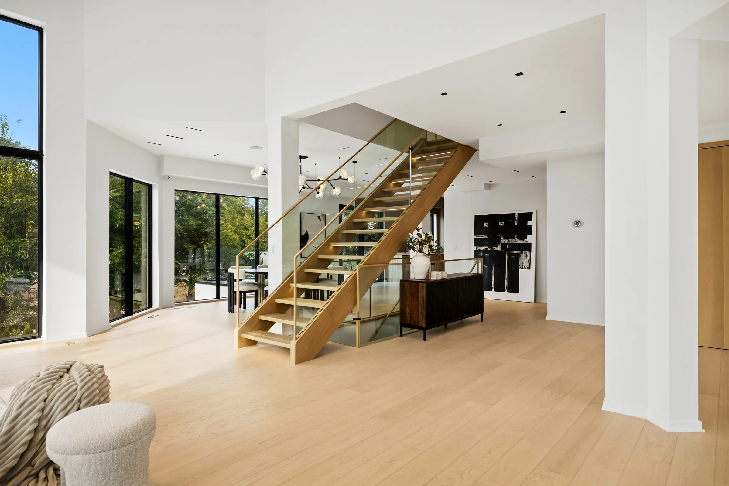 Open oak stair with glass balustrade beside the dining chandelier, seen from the lower hall