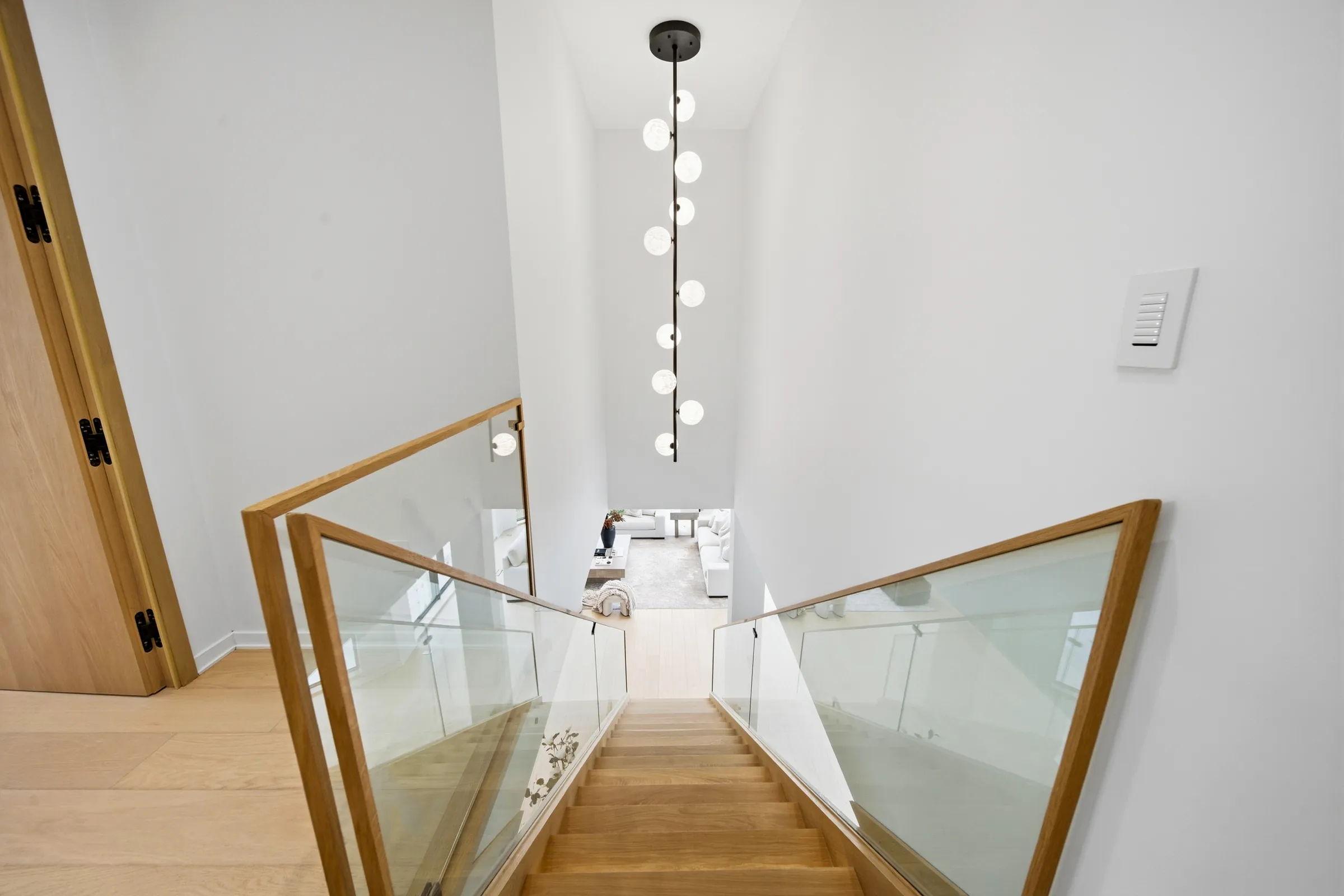 Looking down the oak stair with a vertical string of glass globe pendants dropping through the stairwell