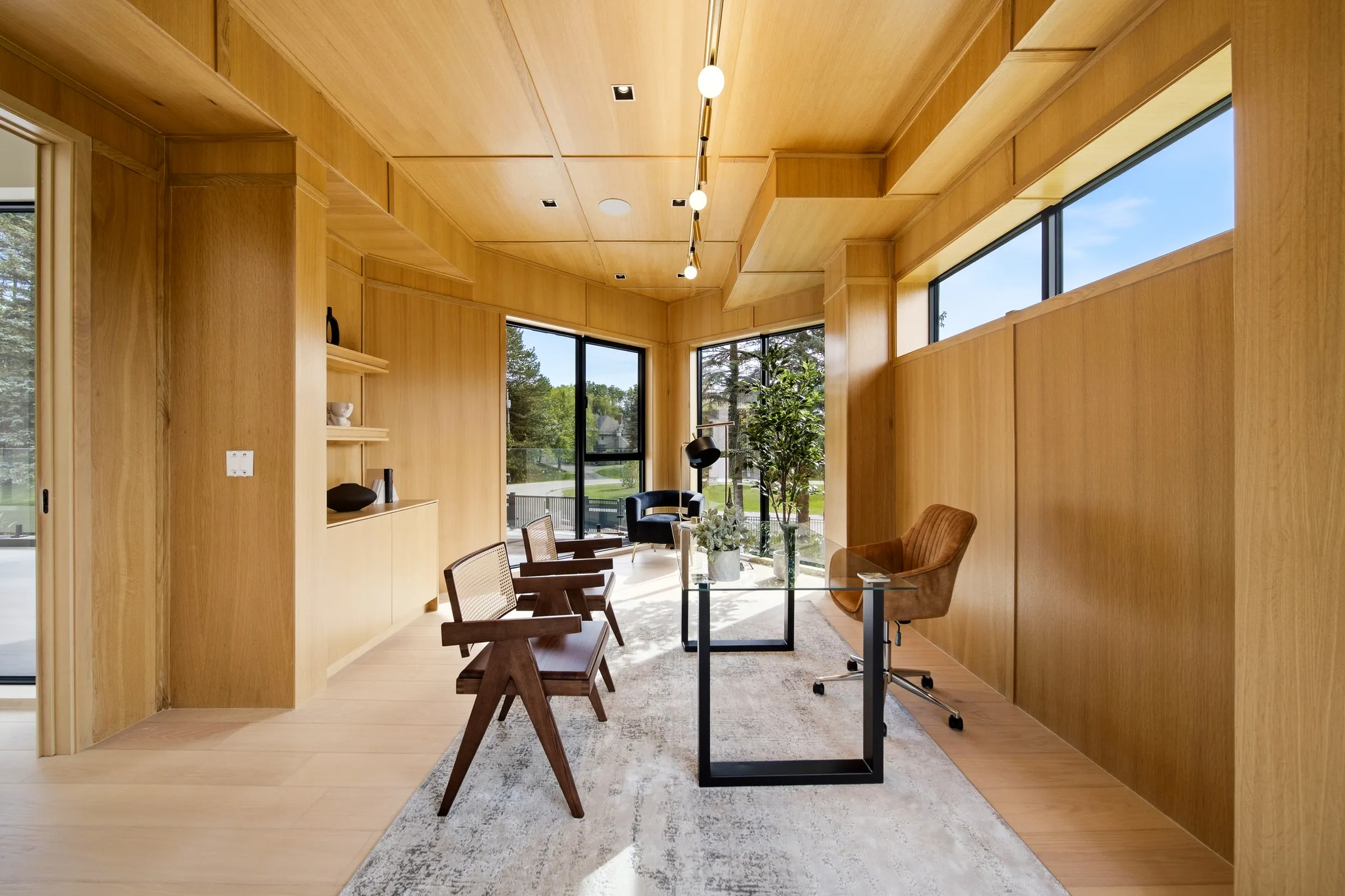 Study with the glass desk under ceiling track spots and shelving lit along the oak wall