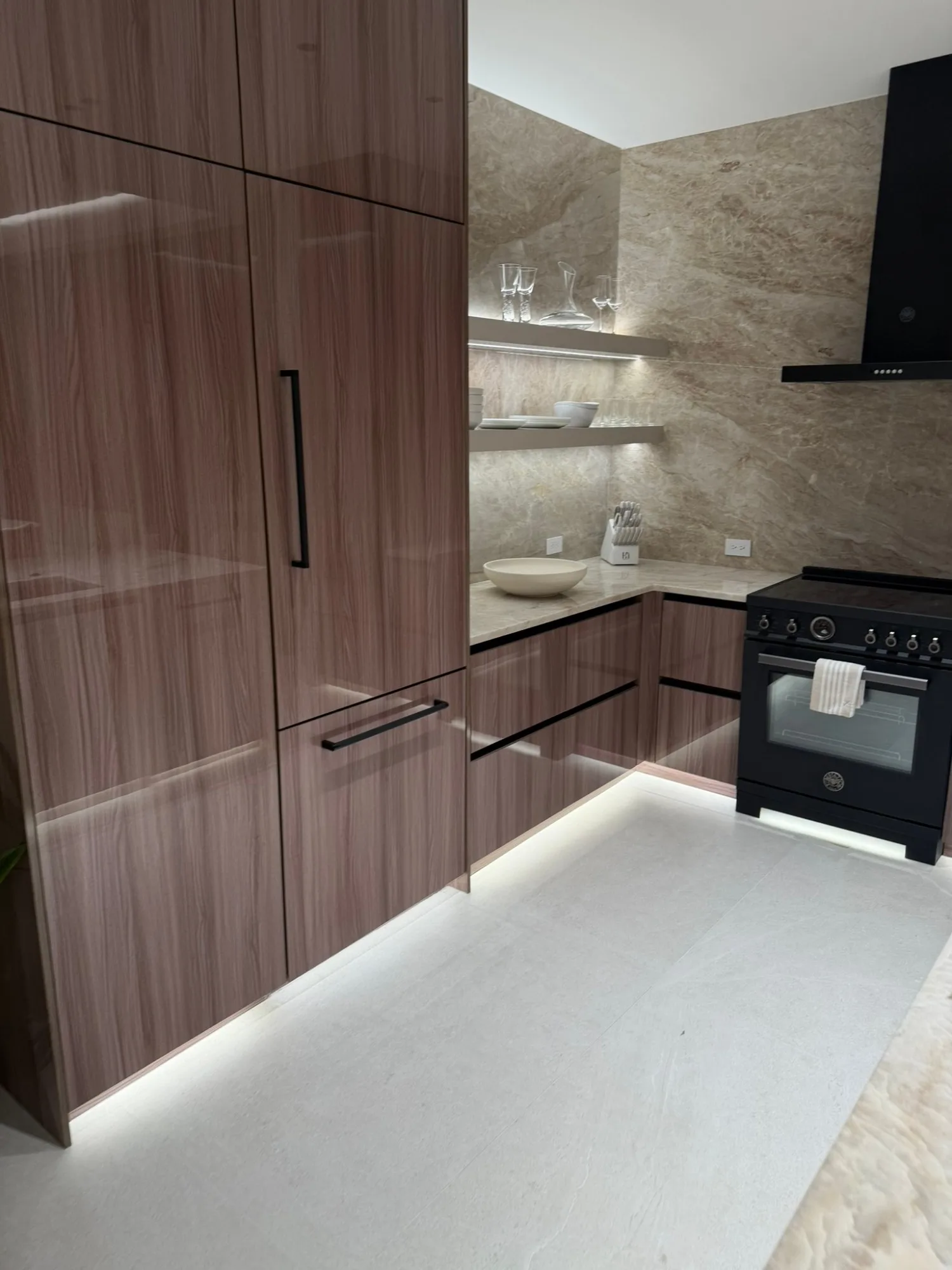 Kitchen in glossy walnut with a lit toe kick and floating stone shelves