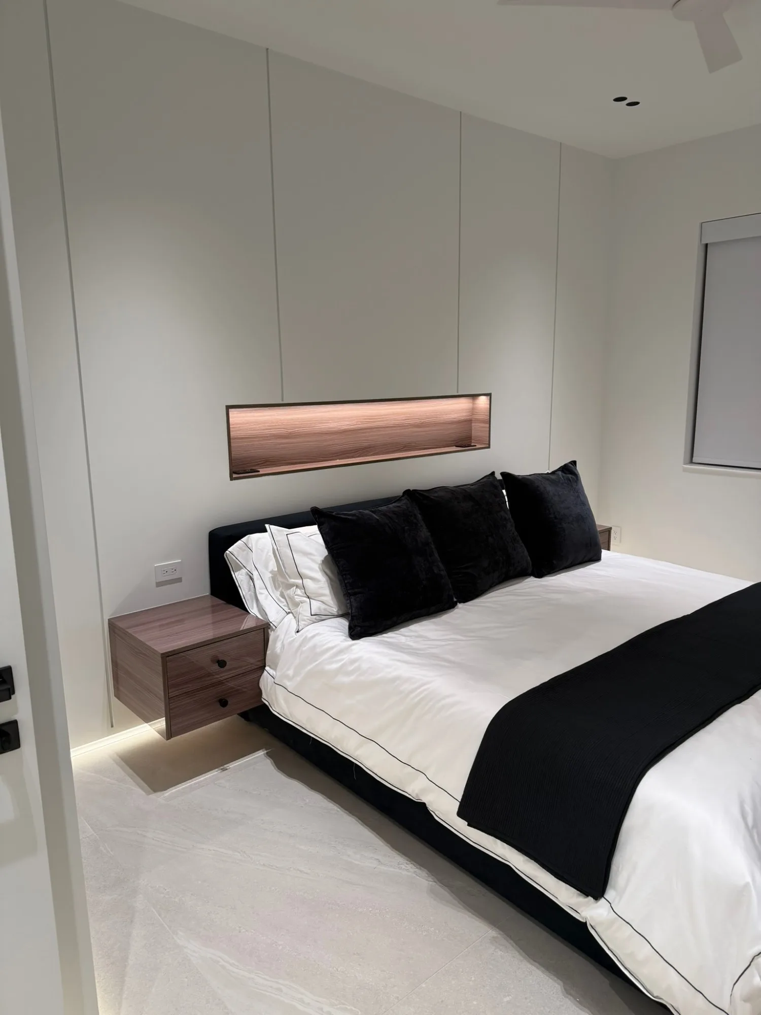 Primary bed under a lit walnut niche, floating nightstand glowing beneath