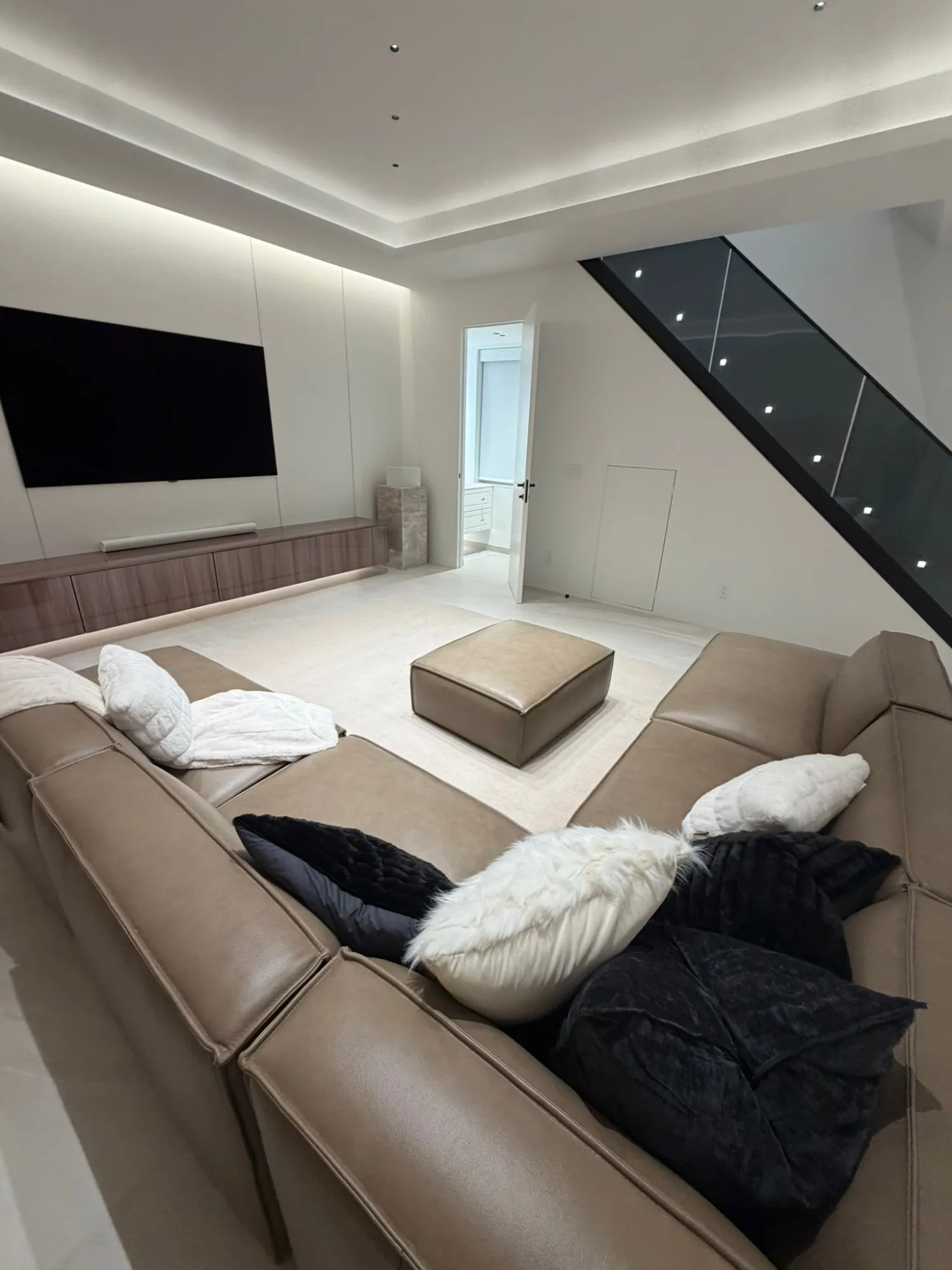 Media room under a lit cove, stair with step lights climbing behind