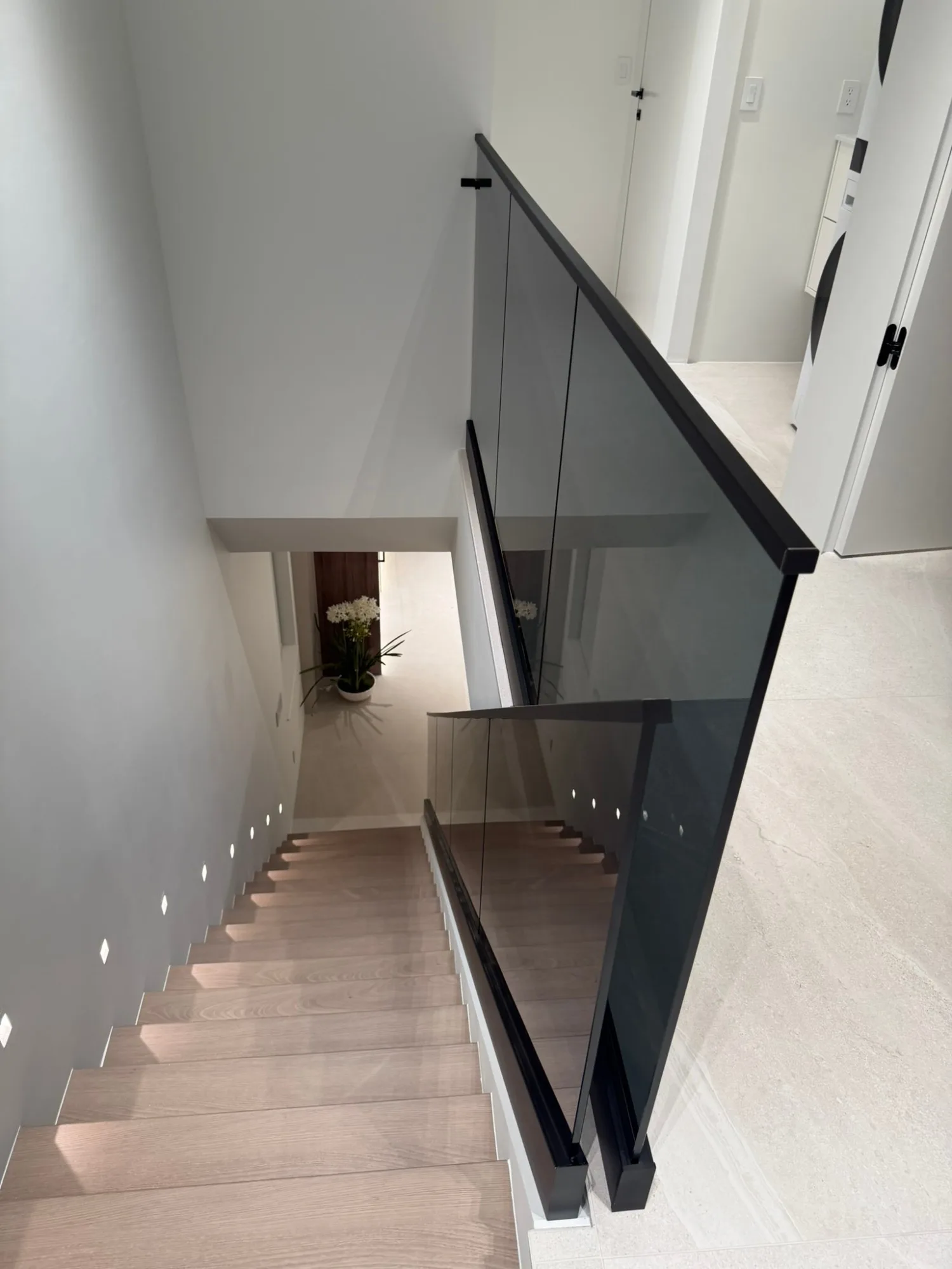 Stair descending past recessed step lights behind a smoked glass rail