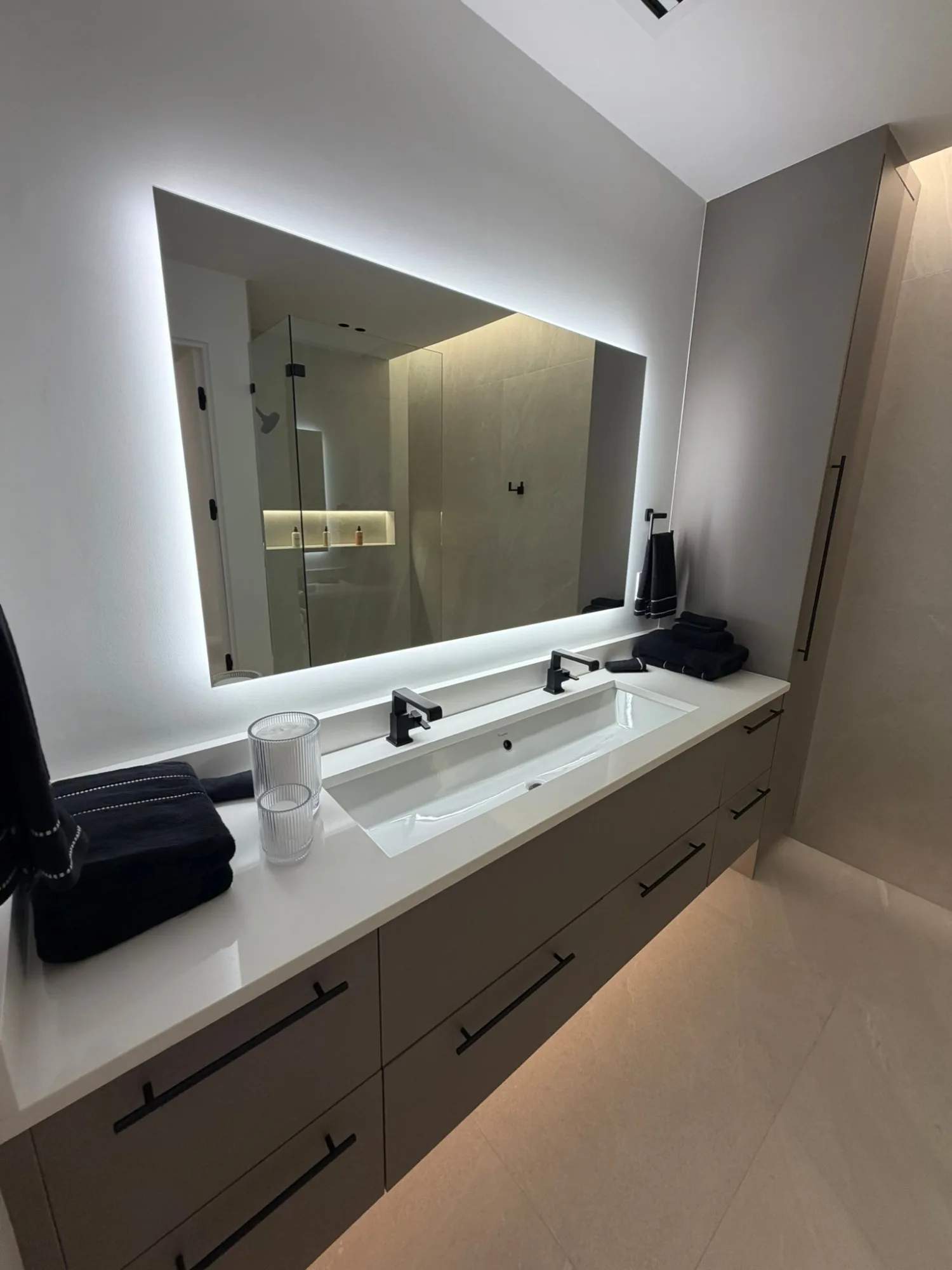 Double vanity under a backlit mirror, cabinets floated on a lit reveal