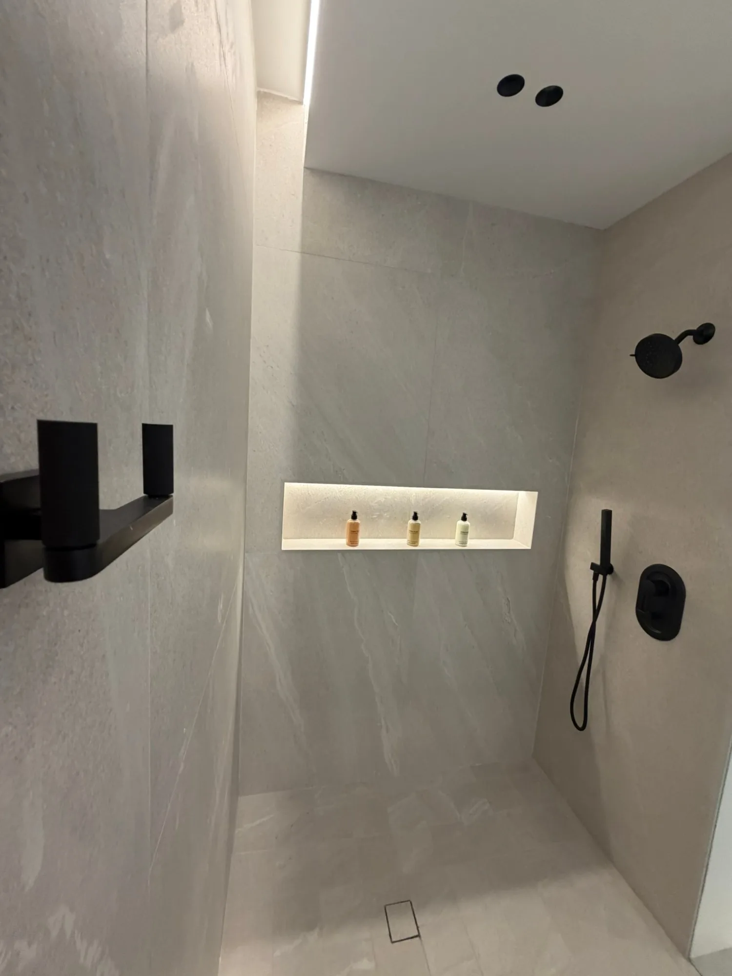 Shower in stone tile with a lit niche and black fittings