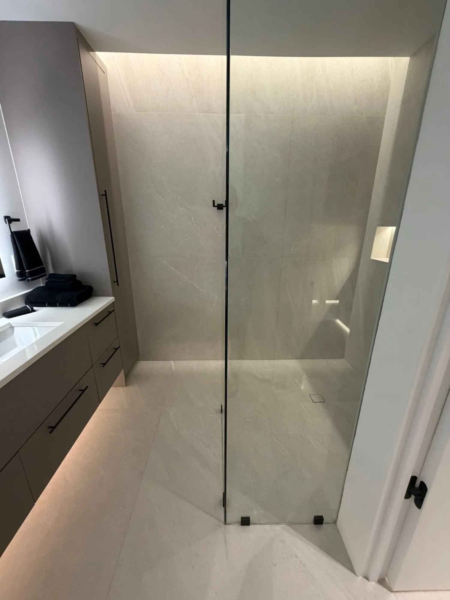 Walk in shower behind frameless glass, washed from a ceiling slot