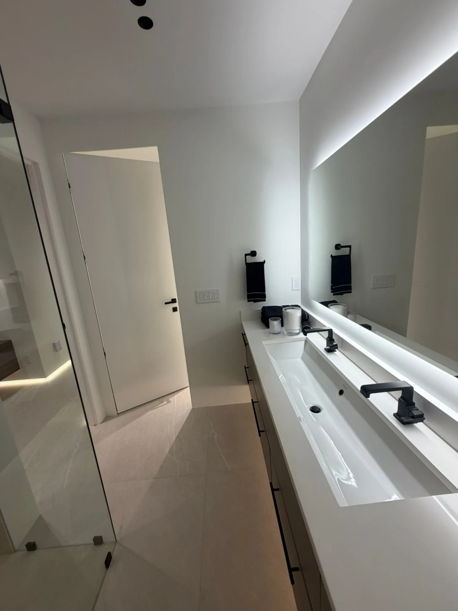 Trough sink with two black faucets under the backlit mirror