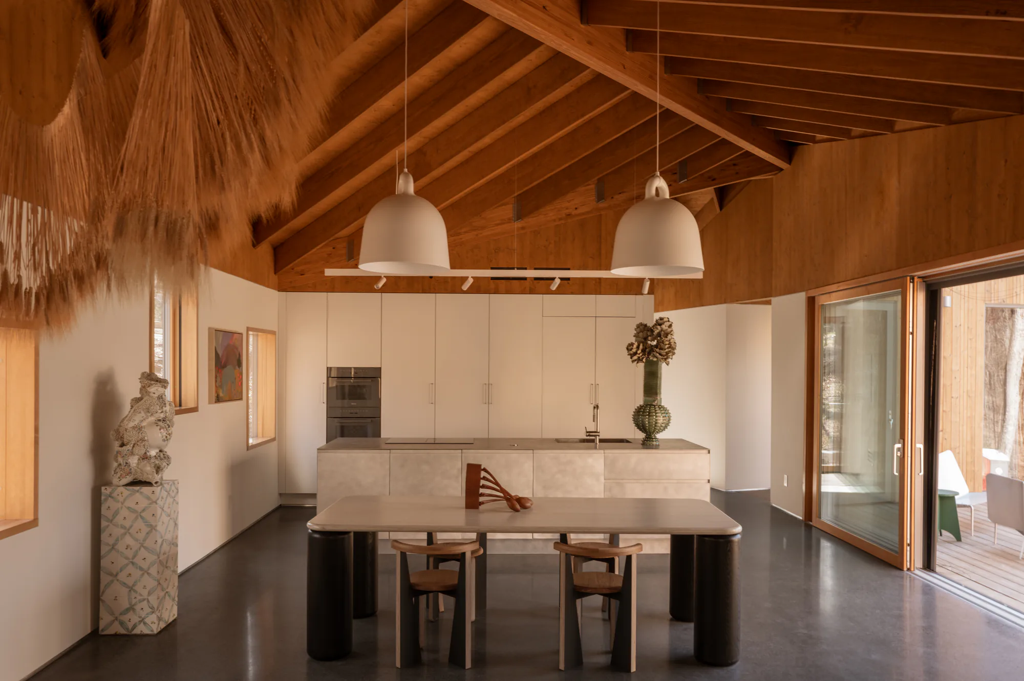 Kitchen and dining under exposed timber rafters, two bell pendants and a track run on the beam