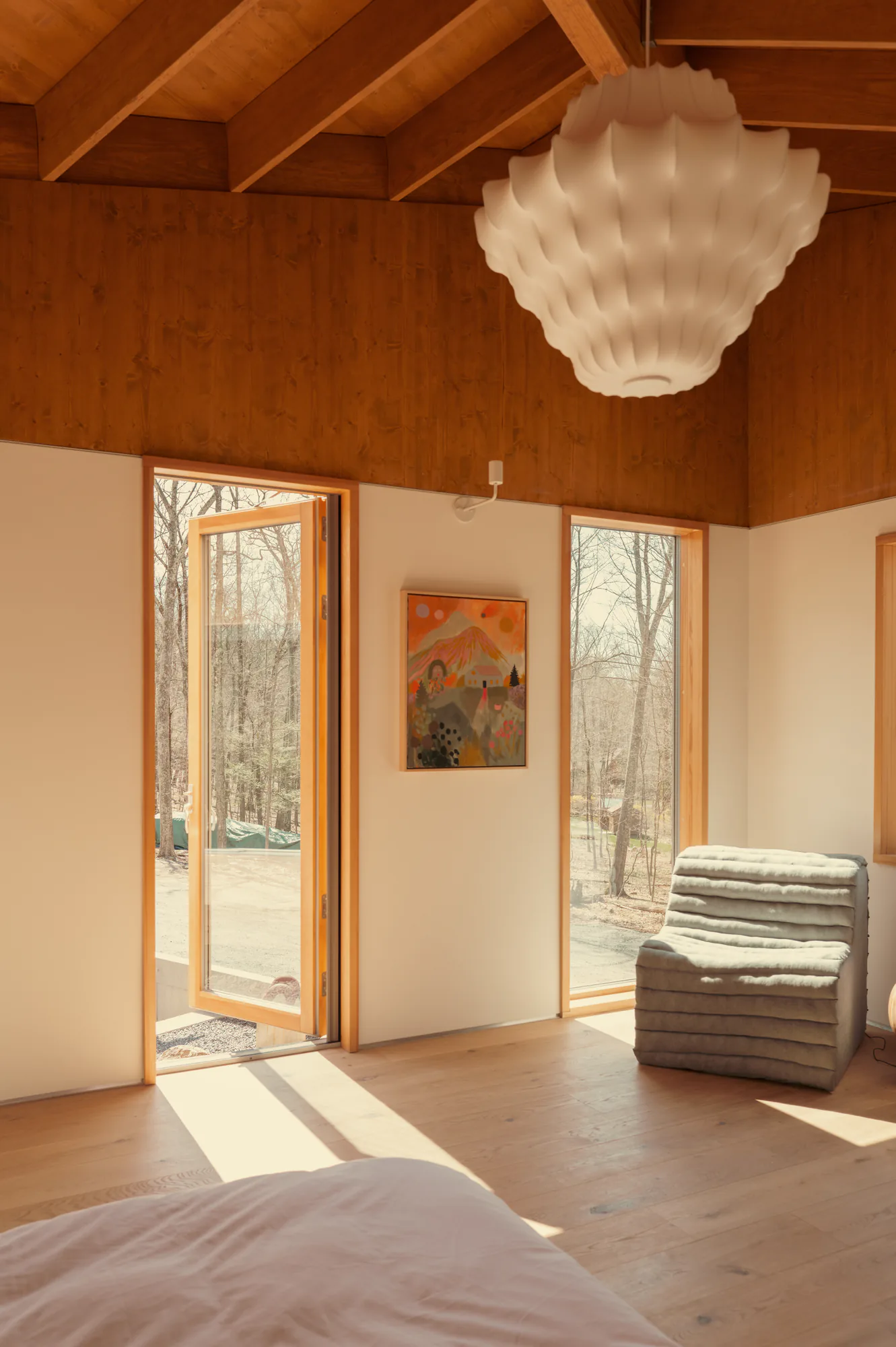 Primary bedroom under the timber ceiling, glazed door open to the deck in low sun